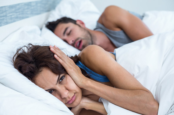 Woman holding a pillow over her ears while her partner snores due to sleep apnea sleeps beside her thankfully she made an appointment at Sleep Apnea Solutions of Cincinnati in Cincinnati, OH