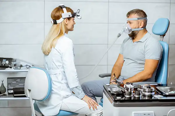 White female doctor assesses a white male patient with a CPAP sleep apnea machine attached to his face.